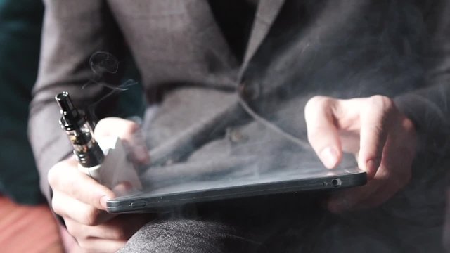 businessman with an e-cigarette and reads his tablet computer shot in slow motion