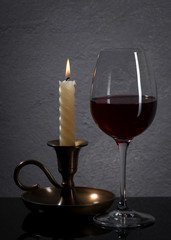Glass. Red wine glass and candle  in front of stone granite wall