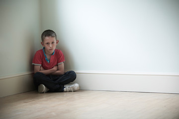 Unhappy Child Sitting In Corner Of Room
