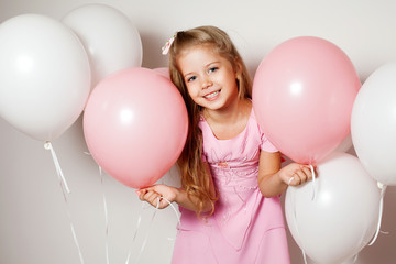 Happy girl with a gift box in the form of heart and white and pink balloons 