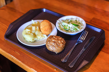 Cutlet, potatoes, salad and bun on the tray in cafe
