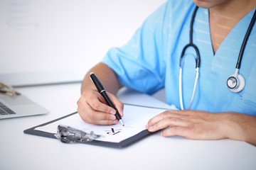 Fototapeta premium Portrait of unknown male surgeon doctor holding his stethoscope and filling up medical prescription