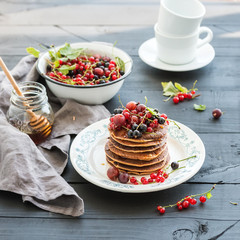 Breakfast set. Buckwheat pancakes with fresh berries and honey on rustic plate over black wooden table