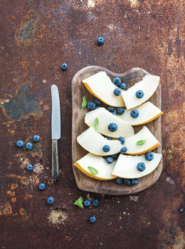 Melon and blueberries in a rustic wooden serving dish over grunge metal rusty background, top view