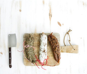 French alsacian smoked salamis on rustic wooden chopping board over white backdrop, top view