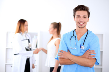 Fototapeta premium Attractive male doctor in front of medical group, crossed arms