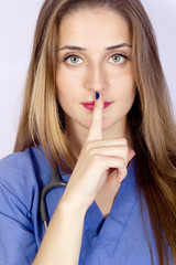 Naklejka premium Young nurse on blue with finger in front of lips for silence.