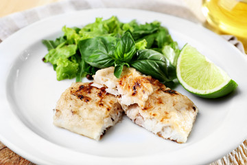 Dish of fish fillet with greens and lime on plate close up