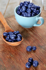 Fresh blueberries in cup and spoon on wooden table close up