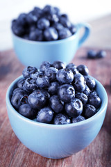 Fresh blueberries in cups on wooden table close up