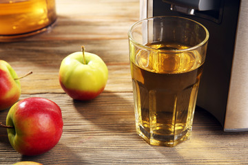 Stainless juice extractor with apples and glass of juice on wooden background, close up