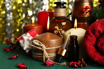 Composition of alight candles, towel and aroma oil on green wooden table against sparkle background