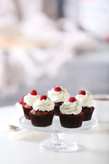 Beautiful chocolate cupcakes with cream and raspberry on table