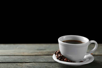 Cup of coffee and coffee grains on wooden table, on gray background