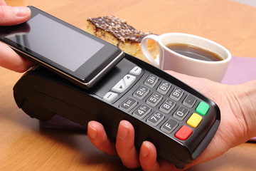 Paying with mobile phone with NFC technology for cheesecake and coffee in cafe, finance concept