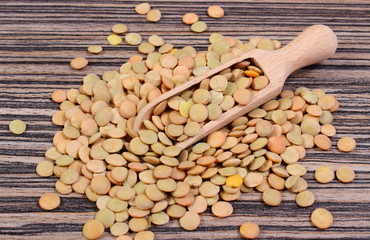 Heap of green lentil with spoon on wooden background
