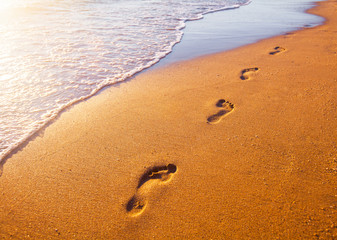 beach, wave and footprints at sunset time