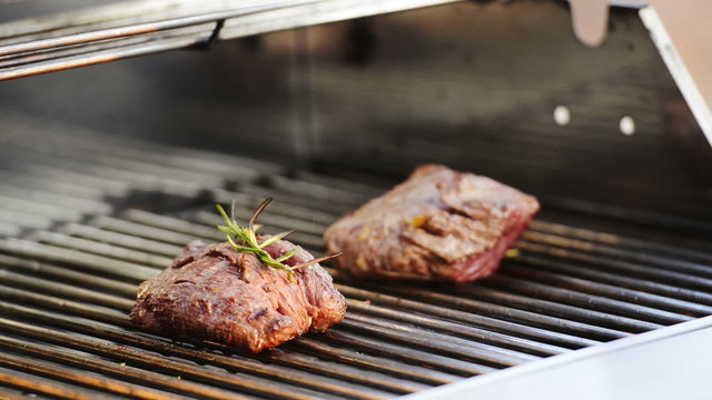 Grilling beef fillet steak on the barbecue or BBQ with a lid opening to check meat. Grilling with olive oil and rosemary in high definition footage