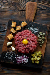 Top view of beef steak tartare on a rustic wooden chopping board