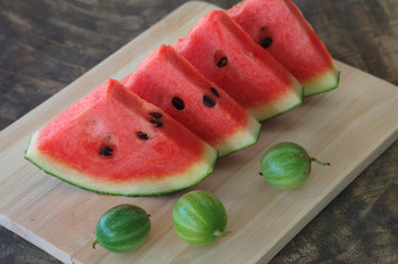 sliced fresh red watermelon and small watermelon on cutting board.