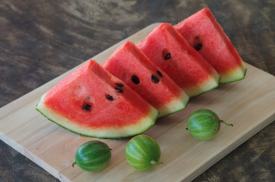 sliced fresh red watermelon and small watermelon on cutting board.
