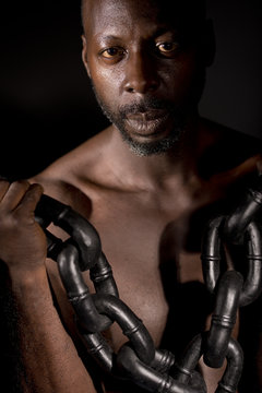 Bare chested black man, holding a heavy chain, shot against a black background.