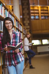 Smiling student leaning against bookshelves reading book