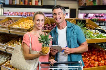 Smiling couple holding a pineapple and a grocery list