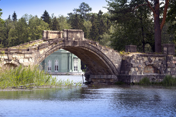 Fototapeta premium The ancient destroyed bridge in park and pavilion of Venus (1793) is visible under a bridge arch. Gatchina, St. Petersburg, Russia