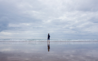 a child running on a vast ocean beach with sky reflected in it