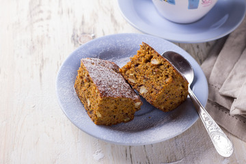Homemade carrot and banana cake with nuts and spices, sprinkled with powdered sugar and a cup of tea on white vintage surface