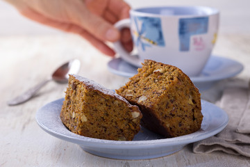 Homemade carrot and banana cake with nuts and spices, sprinkled with powdered sugar and a cup of tea on white vintage surface