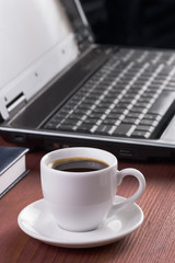 Desktop with coffee cup, opened laptop computer and diary on background, no people, focused on coffee