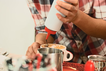 Fototapeta na wymiar Cappuchino preparing. Barista painting over milk foam in cup