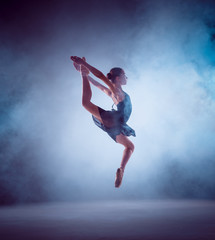 Fototapeta na wymiar The silhouette of young ballet dancer jumping on a blue background