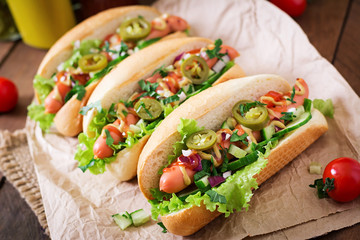 Hot dog with jalapeno peppers, tomato, cucumber and lettuce on wooden background
