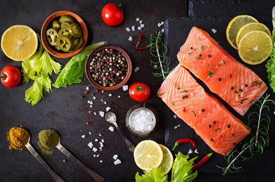 Raw salmon fillet and ingredients for cooking on a dark background in a rustic style. Top view