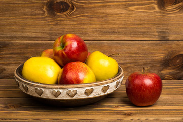 Red and yellow apples on the wooden plate on the rustic background.