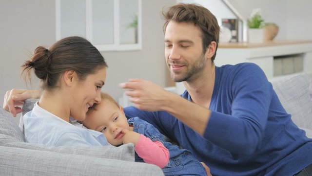 Young parents with baby sitting in sofa at home