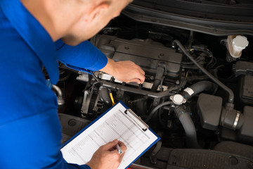 Mechanic Standing Near Car Writing On Clipboard