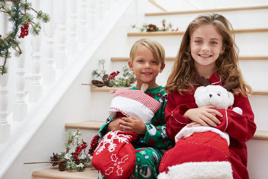 Two Children Sitting On Stairs In Pajamas At Christmas