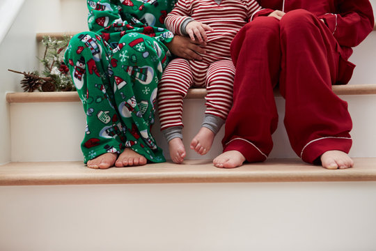 Three Children In Pajamas Sitting On Stairs At Christmas