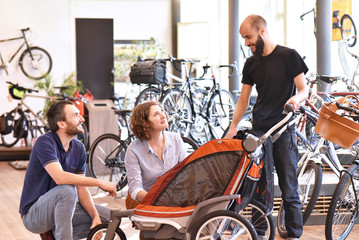 junges Paar mit Verkäufer beim Beratungsgespräch im Einzelhandel - Verkauf Kinderanhänger /...