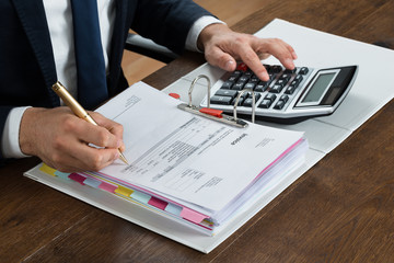 Businessman Using Calculator While Checking Invoice At Desk