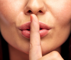 close up of young woman holding finger on lips