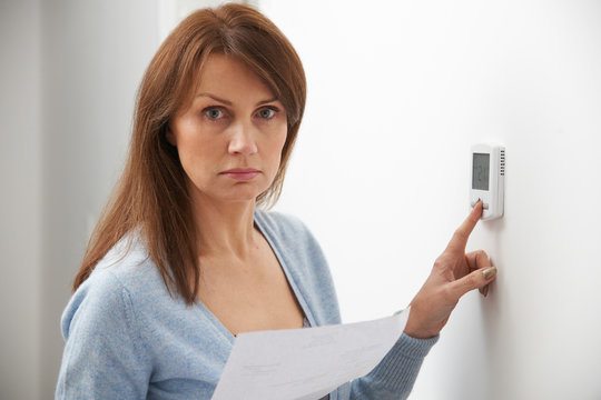 Worried Woman With Heating Bill Turning Down Thermostat