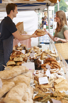 Bread Stall Owner At Market Serving Customer With Loaf