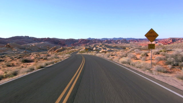 Driving USA: Car driving POV along an empty desert road through the Valley of Fire, Nevada. Beautiful desert landscape and views to distant sandstone mountains
