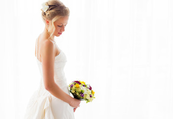 Bride standing by the window in her wedding dress and bouquet