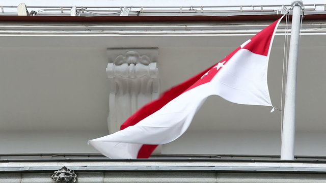 Singapore flag waves in wind from flagpole on top of building